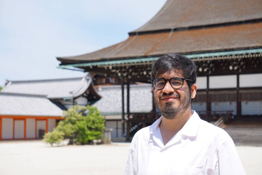 Portrait of Nikolas Tapia, a postdoctoral researcher at the Weierstrass Institute. He is standing in front of a traditional Japanese building, wearing glasses and a white shirt, and smiling at the camera.